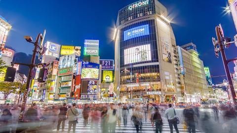 Blurred image of downtown Tokyo at night with people walking across the street.