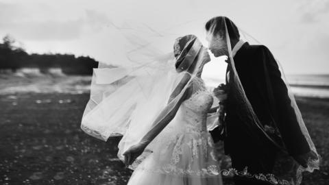 Black and white image of a bride and groom kissing on a beach