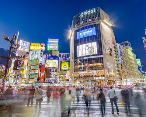 Blurred image of downtown Tokyo at night with people walking across the street.
