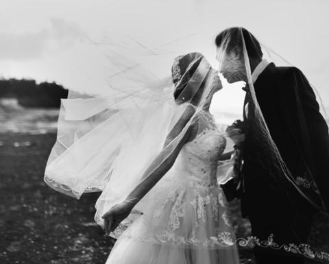 Black and white image of a bride and groom kissing on a beach